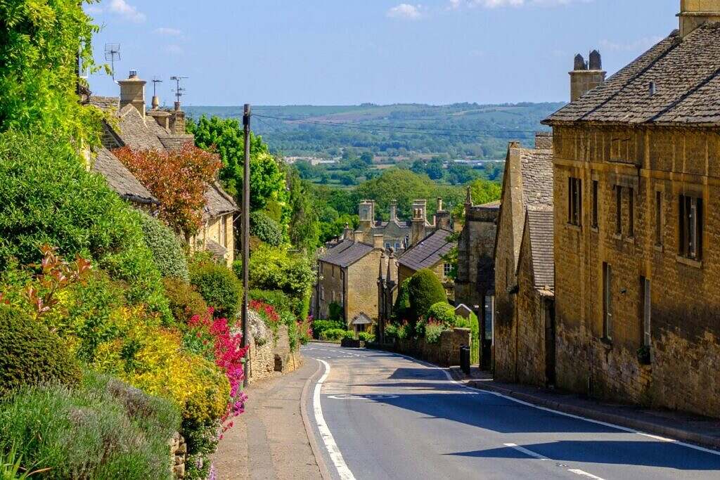 Cotswold Village i Sydvästra England. En charmig liten by med gröna kullar i bakgrunden.
