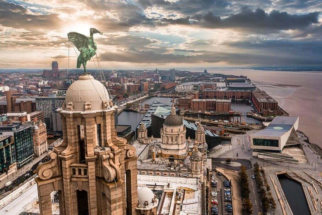 Liverpool Royal Liver Building fotograferad uppifrån med en fågelskulptur högt uppe på ett torn och resten av hamnen och havet i bakgrunden.