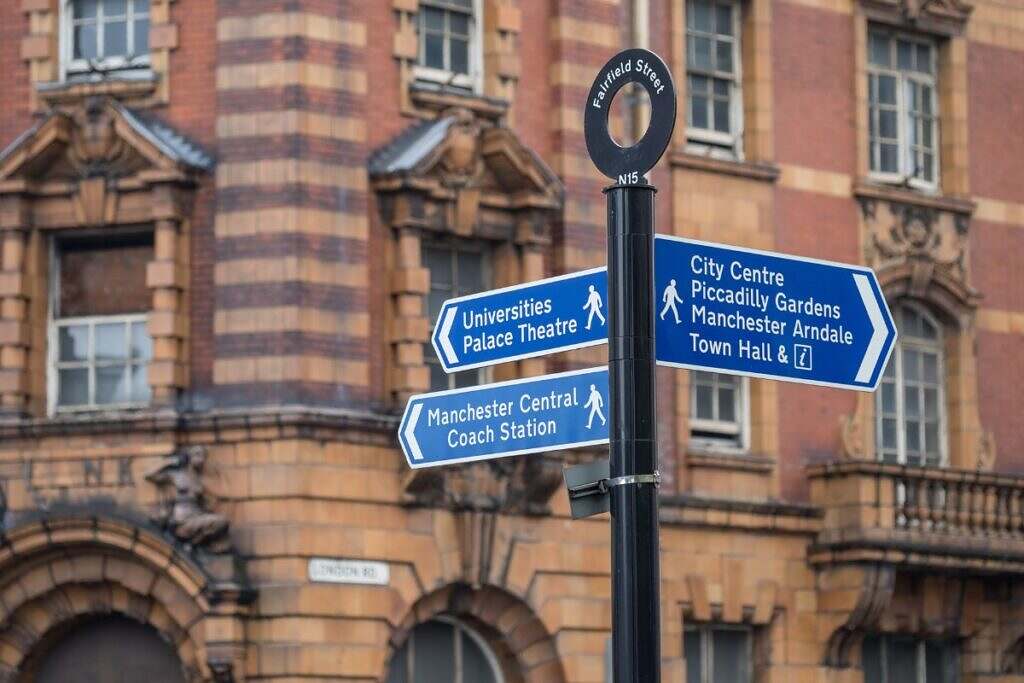 En skylt i Manchester som visar riktningen till Manchester tågcentral, Town Hall, Universitetet, och Piccadilly Gardens.