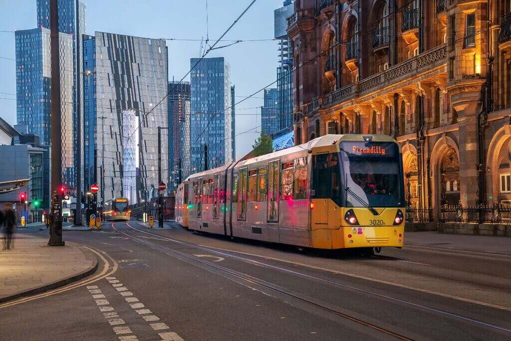 En modern spårvagn med nya skyskrapor bakom sig på ena sidan, och the Midland Hotel, ett äldre vackert tegelstenshus med rundade fönster, på andra sidan.