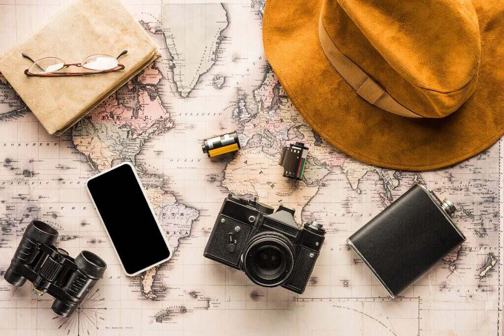 En hatt, plunta, gammal kamera med film, kikare och en mobil ligger på en världskarta.