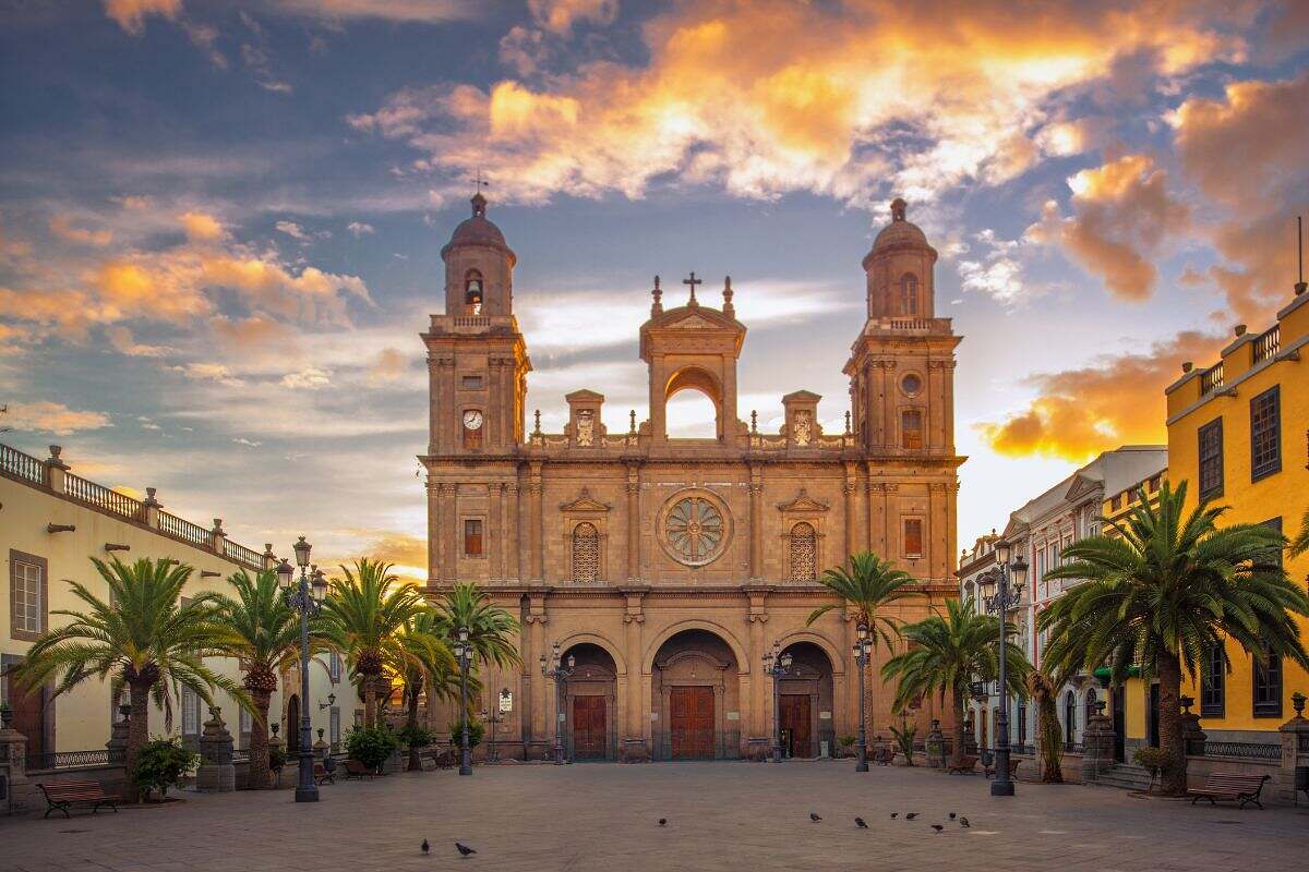 En vacker gammal katedral på Gran Canaria, Spanien med palmer utanför och en dramatisk himmel.