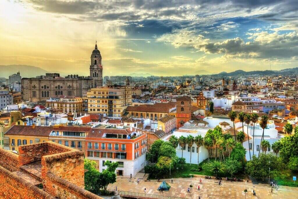 En vy över den vackra staden Malaga, Spanien, med dramatiska moln och berg i bakgrunden.