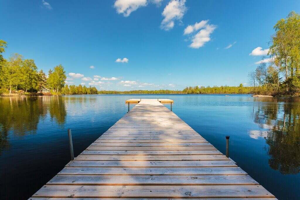 En klassisk svensk, lång brygga leder ut i en stilla sjö med lummiga träd runtomkring.