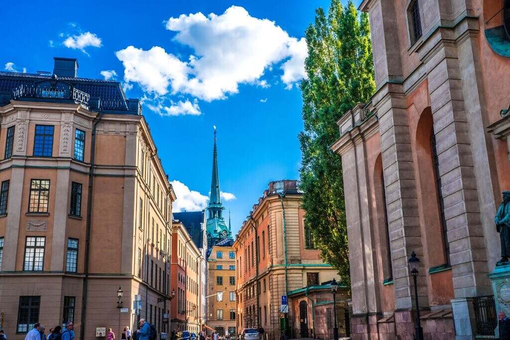 Gamla Stan i Stockholm med vackra byggnader, ett kyrktorn och en blå himmel med vita små moln.