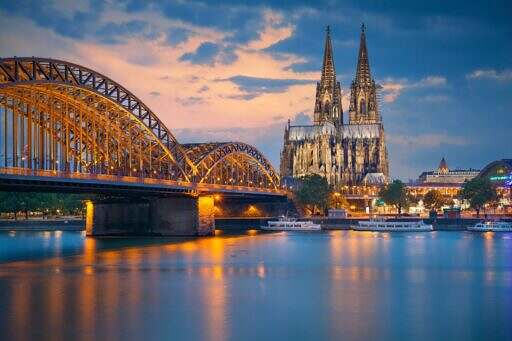 Kölnerdomen i Köln, Tyskland vid floden Rhen och en bro i skymningen.
